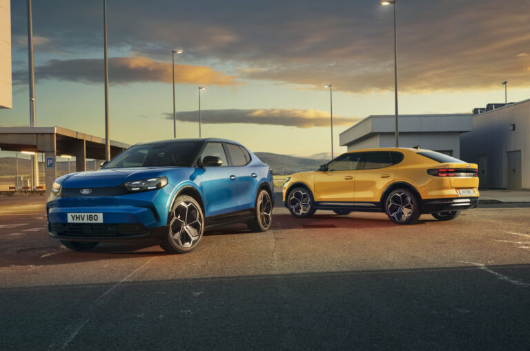 a blue ford capri parked next to a yellow ford capri in an industrial setting at sunset